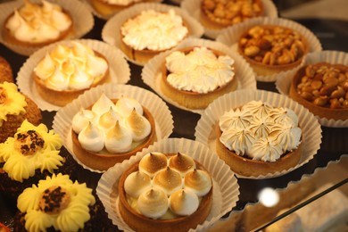 Photo of Different tasty tartlets on counter in bakery shop, closeup
