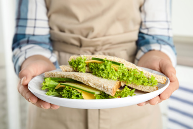 Photo of Woman holding plate with tasty sandwiches indoors, closeup