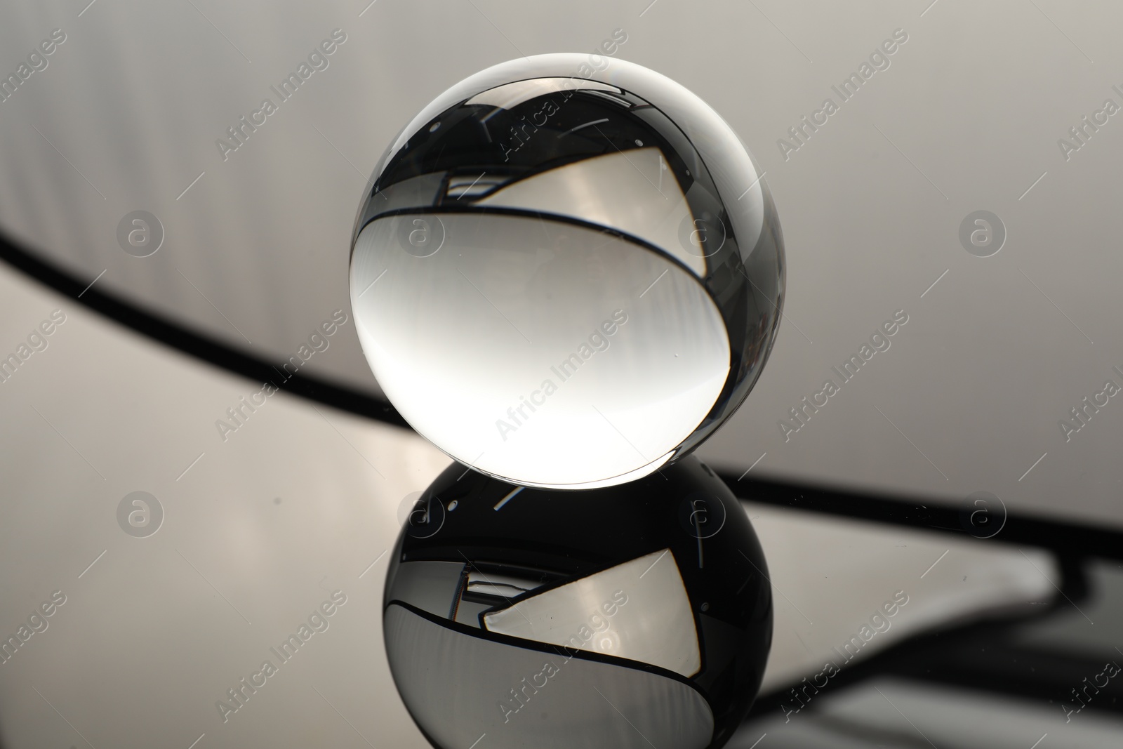 Photo of Transparent glass ball on mirror surface, closeup