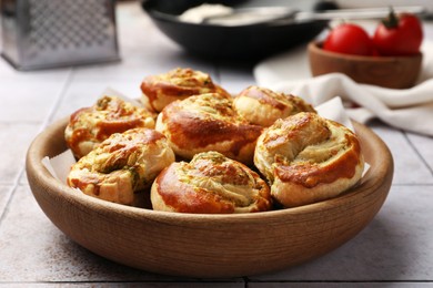 Fresh delicious puff pastry with tasty filling in wooden bowl on white tiled surface, closeup