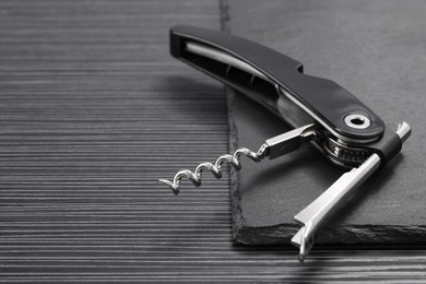 Photo of One corkscrew (sommelier knife) on black wooden table, closeup. Space for text