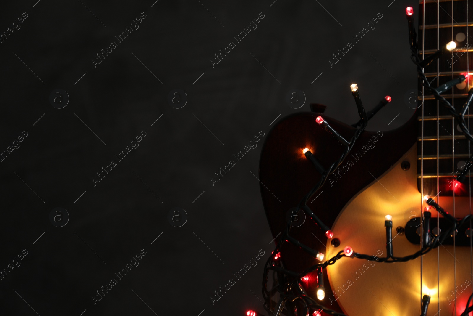 Photo of Guitar with festive lights on dark background, space for text. Christmas music