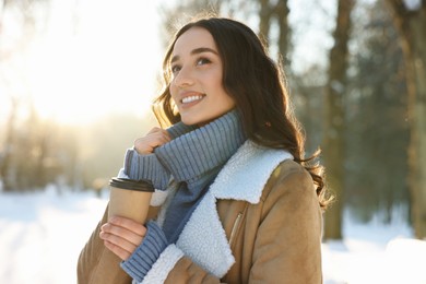 Portrait of smiling woman with paper cup of coffee in snowy park