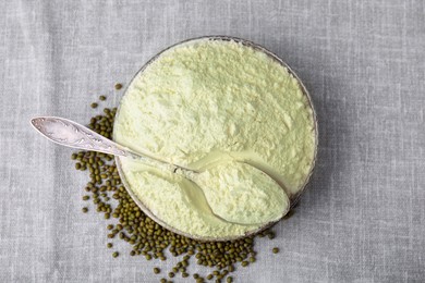 Photo of Bowl of flour, spoon and mung beans on light grey cloth, top view