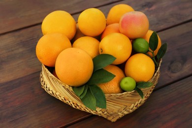Photo of Wicker basket with different citrus fruits and leaves on wooden table
