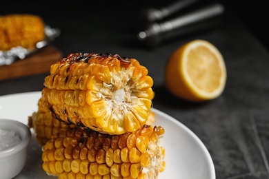 Plate with delicious grilled corn cobs and salt on gray table