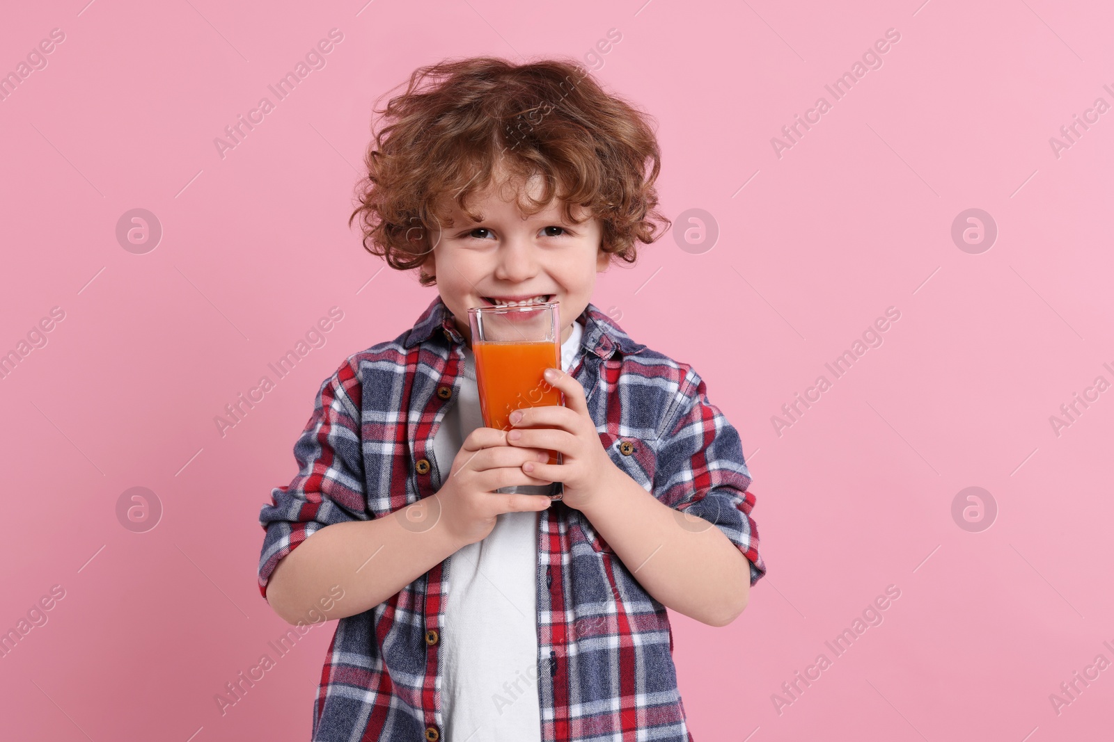 Photo of Cute little boy with glass of fresh juice on pink background