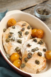 Photo of Delicious chicken fillets with capers, tomatoes and sauce in baking dish on table, closeup