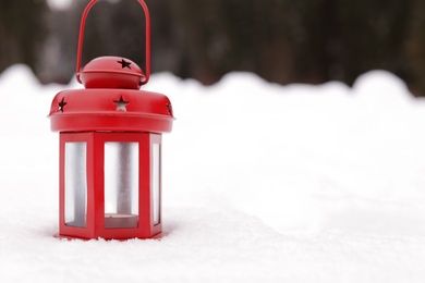 Red lantern with candle on white snow outdoors, space for text. Winter holiday