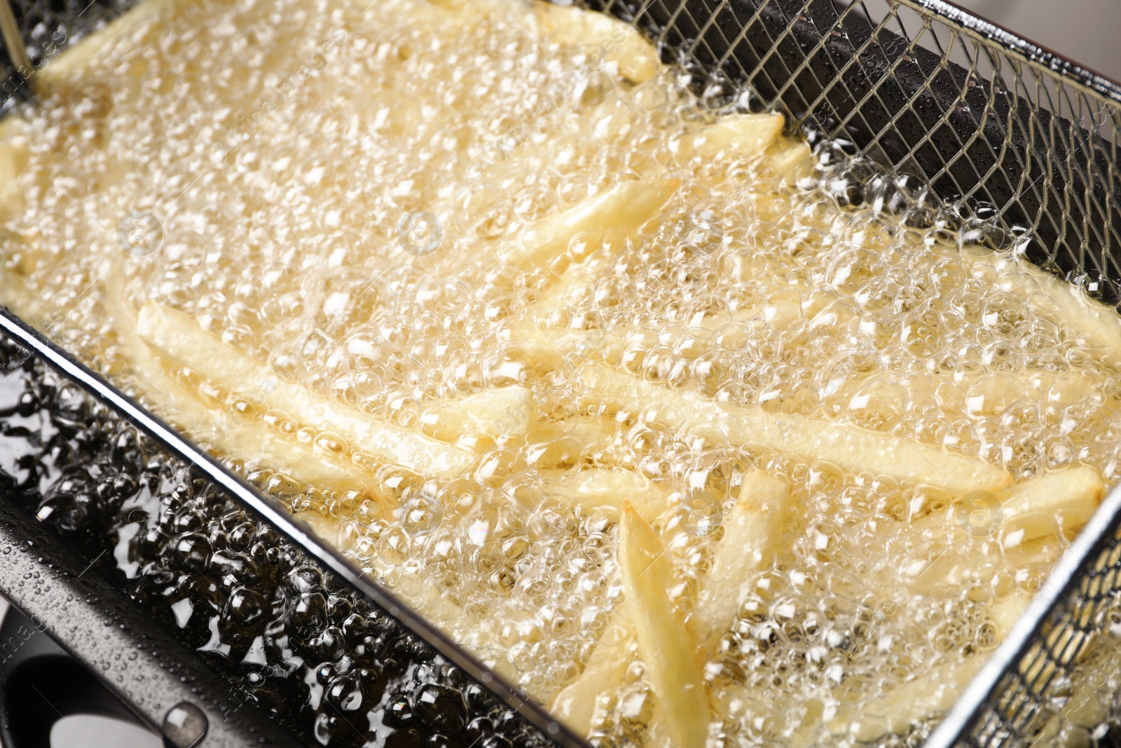 Photo of Cooking delicious french fries in hot oil, closeup