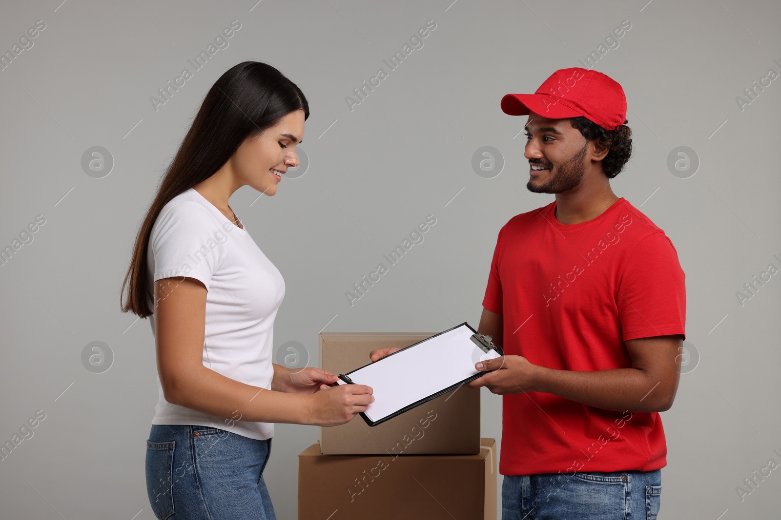 Photo of Smiling woman signing order receipt on grey background. Courier delivery