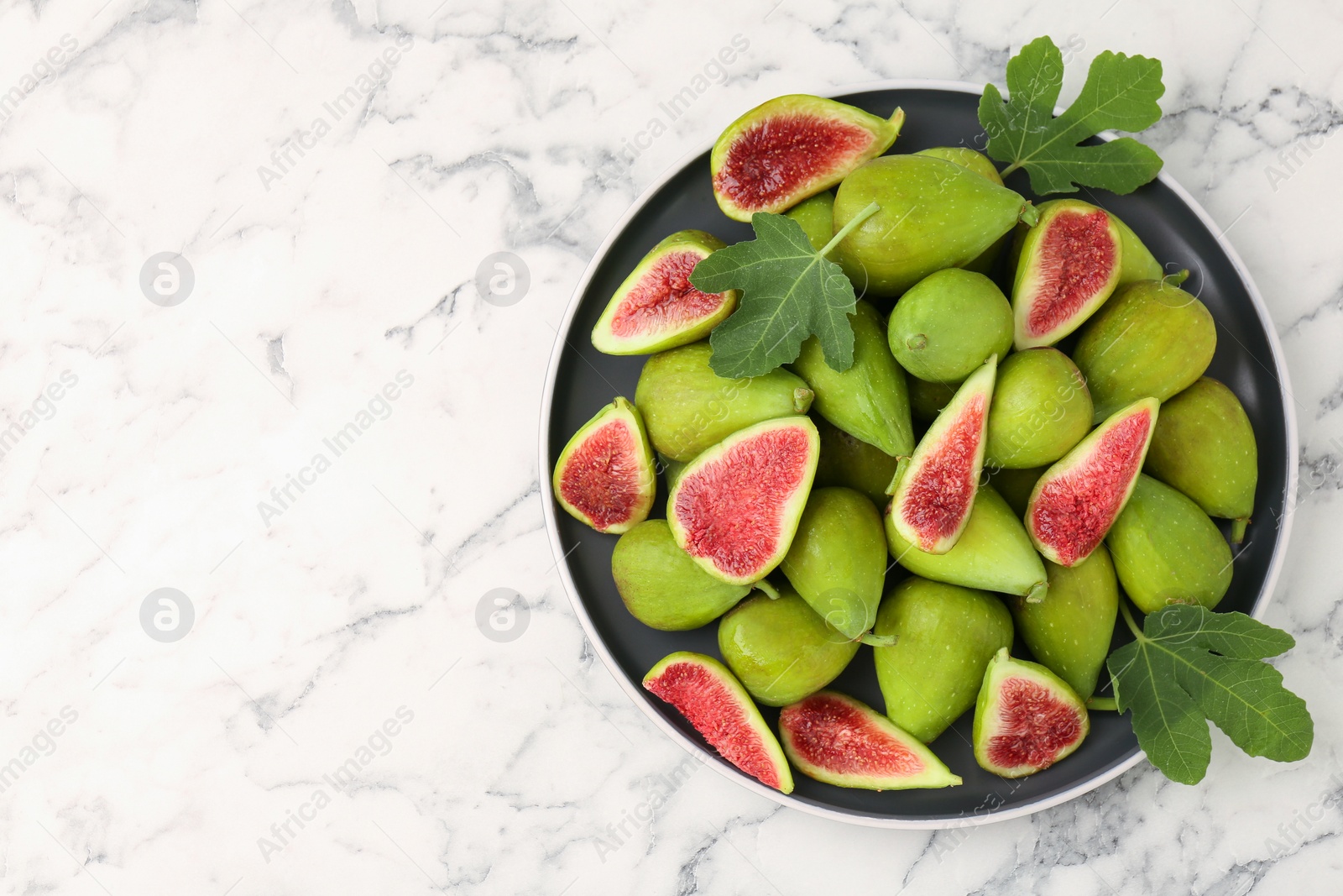 Photo of Cut and whole green figs on white marble table, top view. Space for text