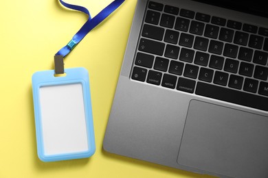 Photo of Blank badge and laptop on yellow background, top view