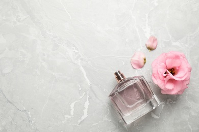 Flat lay composition with bottle of perfume and eustoma flower on light grey marble background, space for text