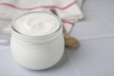 Delicious natural yogurt in glass jar on white tiled table, closeup. Space for text