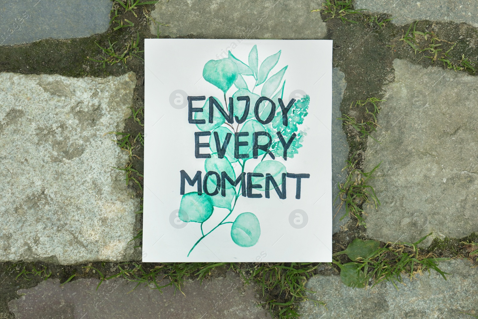 Photo of Card with phrase Enjoy Every Moment on ground, top view