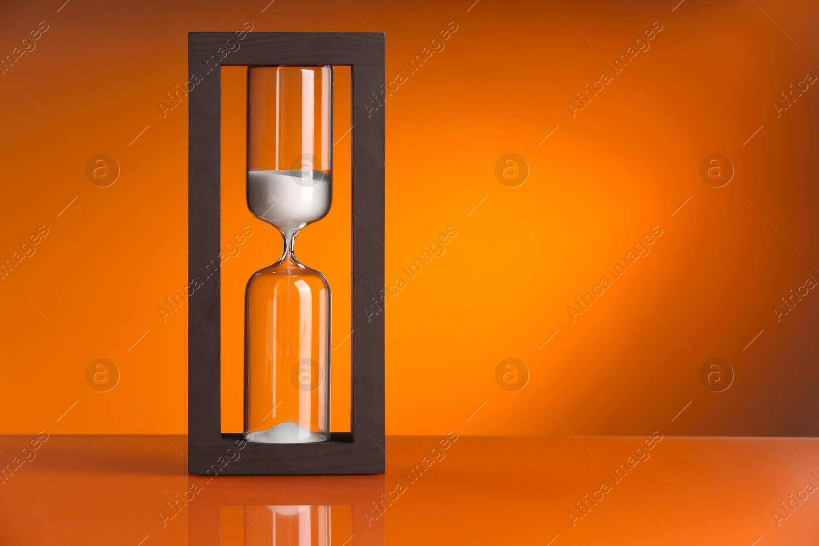 Photo of Hourglass with flowing sand on color background. Space for text