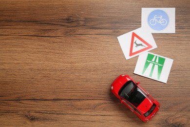 Different road sign cards and toy car on wooden table, flat lay with space for text. Driving school