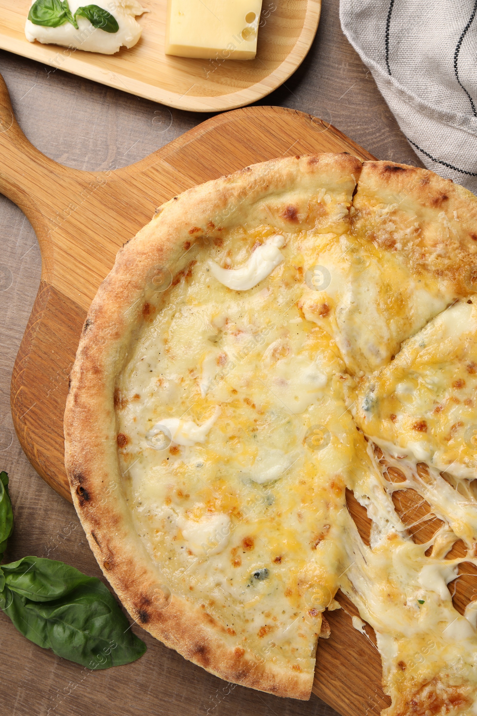 Photo of Delicious cut cheese pizza, basil and different kinds of cheese on wooden table, flat lay