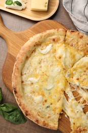 Photo of Delicious cut cheese pizza, basil and different kinds of cheese on wooden table, flat lay