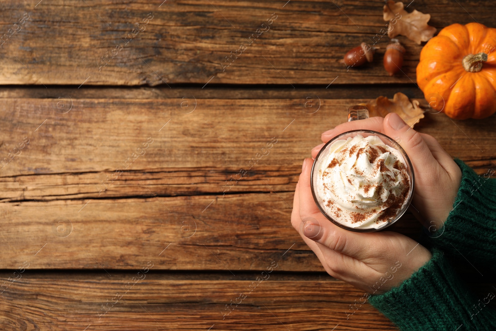 Photo of Woman holding tasty pumpkin latte at wooden table, top view. Space for text