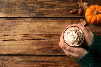 Woman holding tasty pumpkin latte at wooden table, top view. Space for text