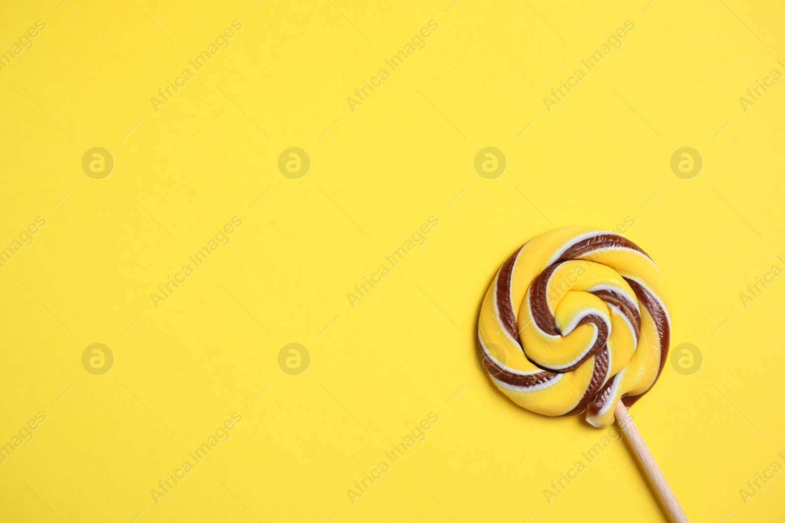 Photo of Stick with colorful lollipop swirl on yellow background, top view. Space for text