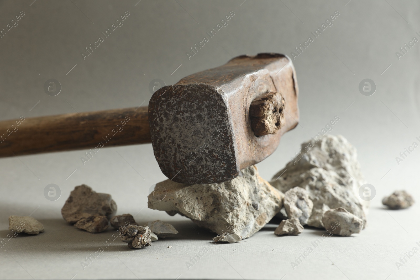 Photo of One sledgehammer and pieces of broken stones on grey background, closeup