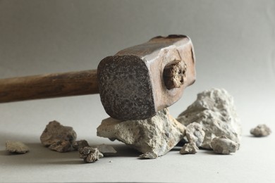 Photo of One sledgehammer and pieces of broken stones on grey background, closeup