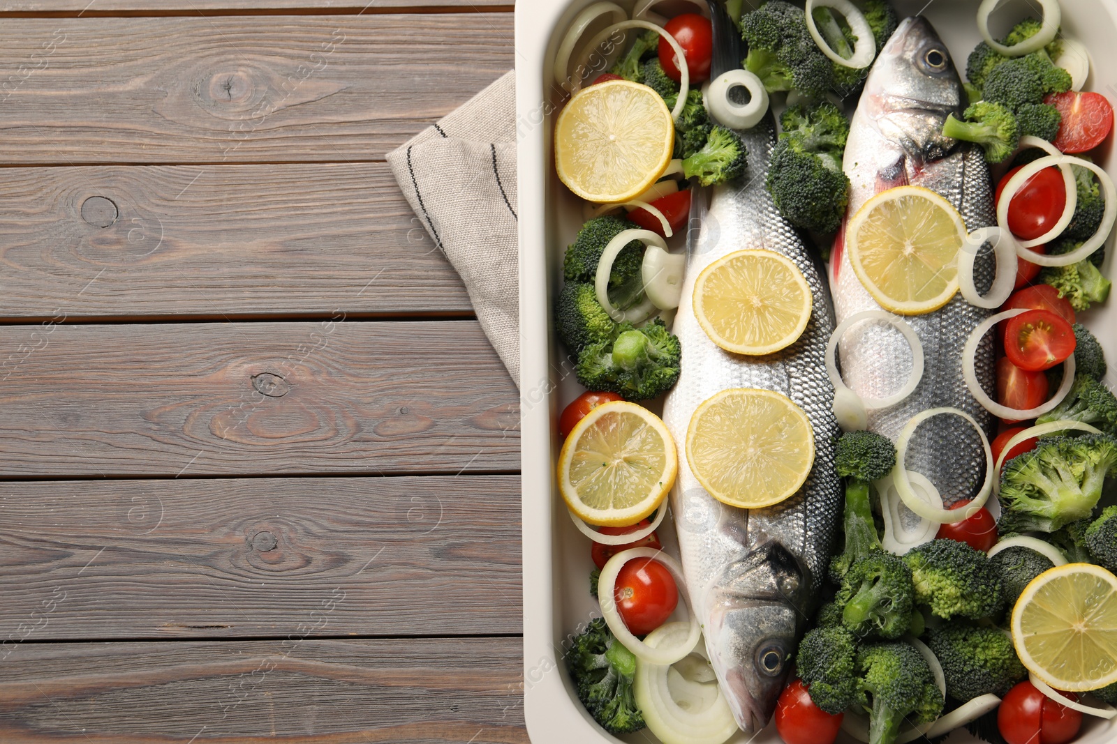 Photo of Raw fish with vegetables and lemon in baking dish on wooden table, top view. Space for text