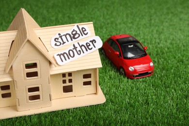 Photo of House model, toy car and text Single Mother on green grass