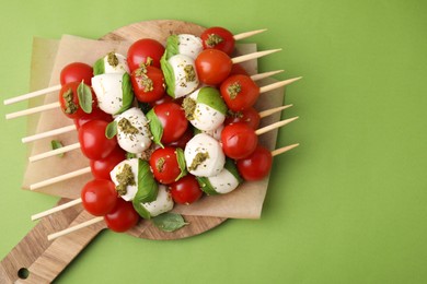 Photo of Caprese skewers with tomatoes, mozzarella balls, basil and pesto sauce on green background, top view. Space for text