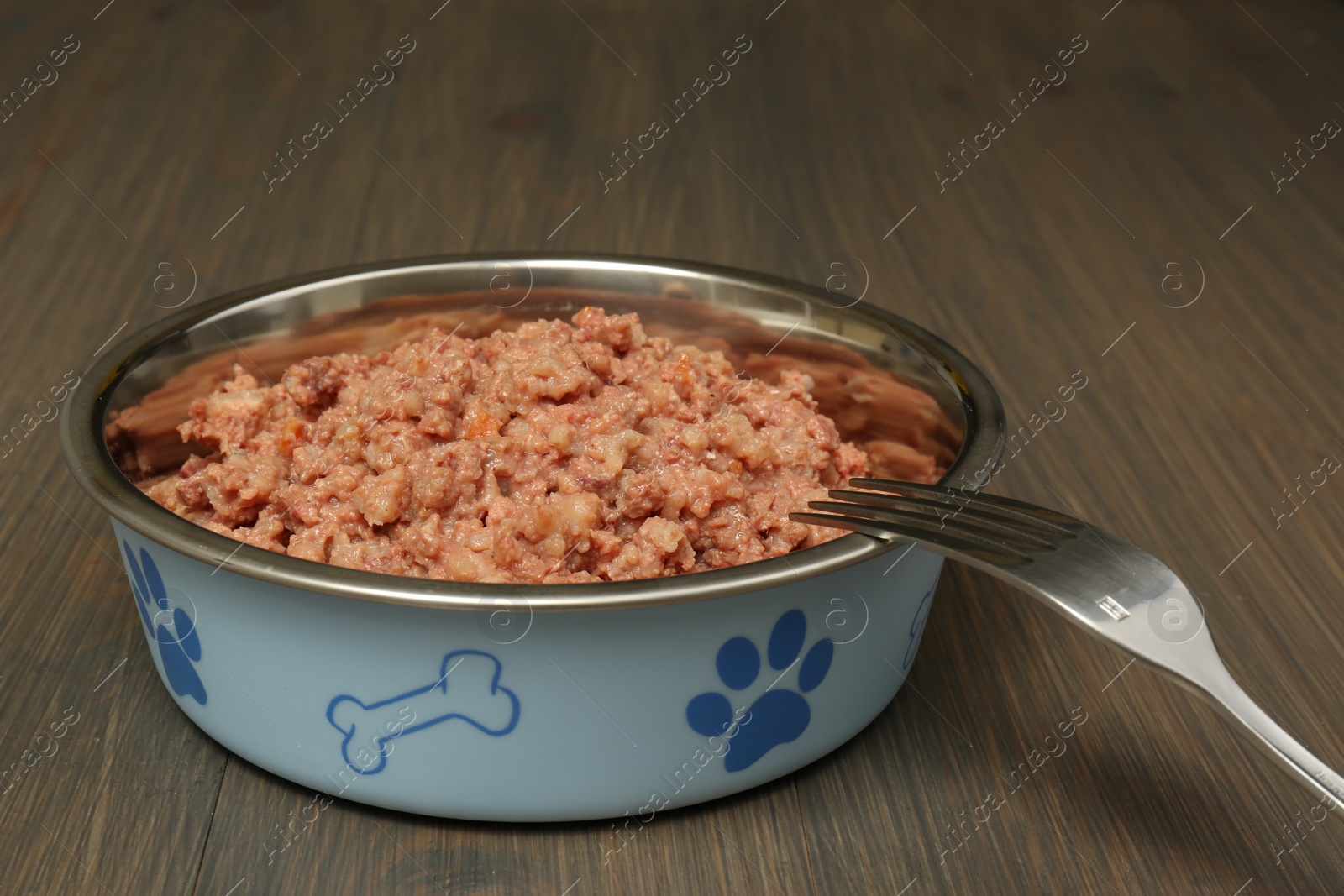 Photo of Bowl of wet pet food with fork on wooden background