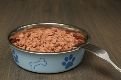 Photo of Bowl of wet pet food with fork on wooden background