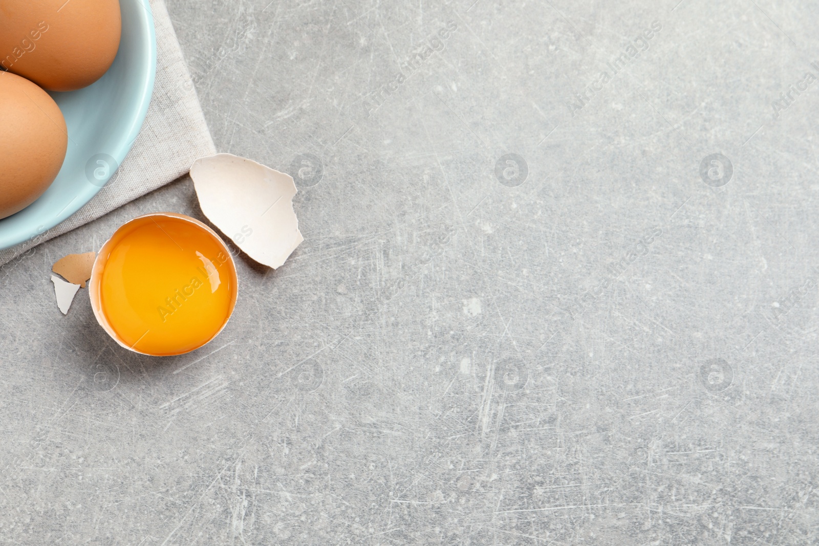 Photo of Raw chicken eggs and shell with yolk on light grey table, flat lay. Space for text