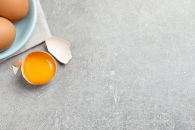 Photo of Raw chicken eggs and shell with yolk on light grey table, flat lay. Space for text