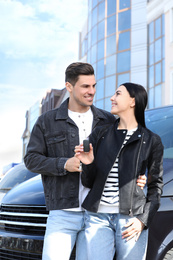 Happy couple with key near car on city street. Buying new auto