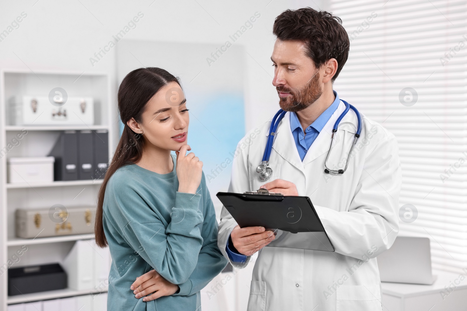 Photo of Doctor with clipboard consulting patient during appointment in clinic