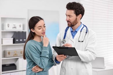 Doctor with clipboard consulting patient during appointment in clinic