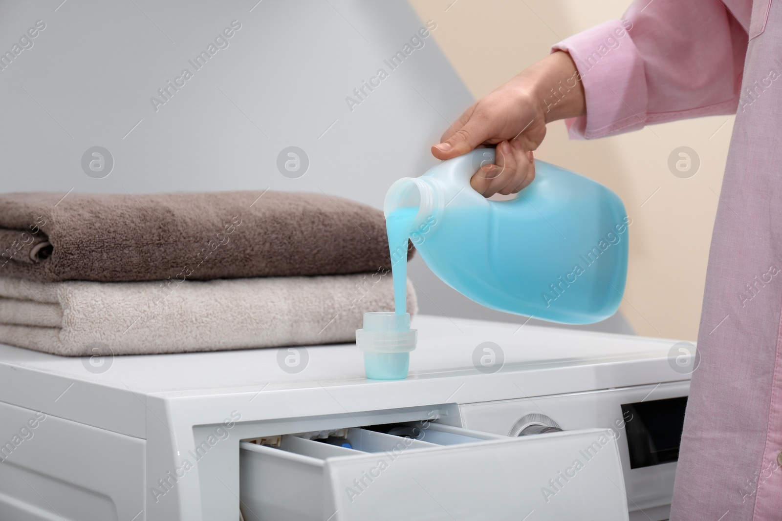 Photo of Woman pouring laundry detergent into cap on washing machine indoors, closeup