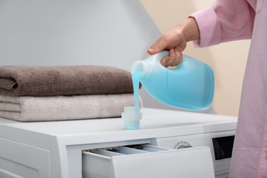 Woman pouring laundry detergent into cap on washing machine indoors, closeup