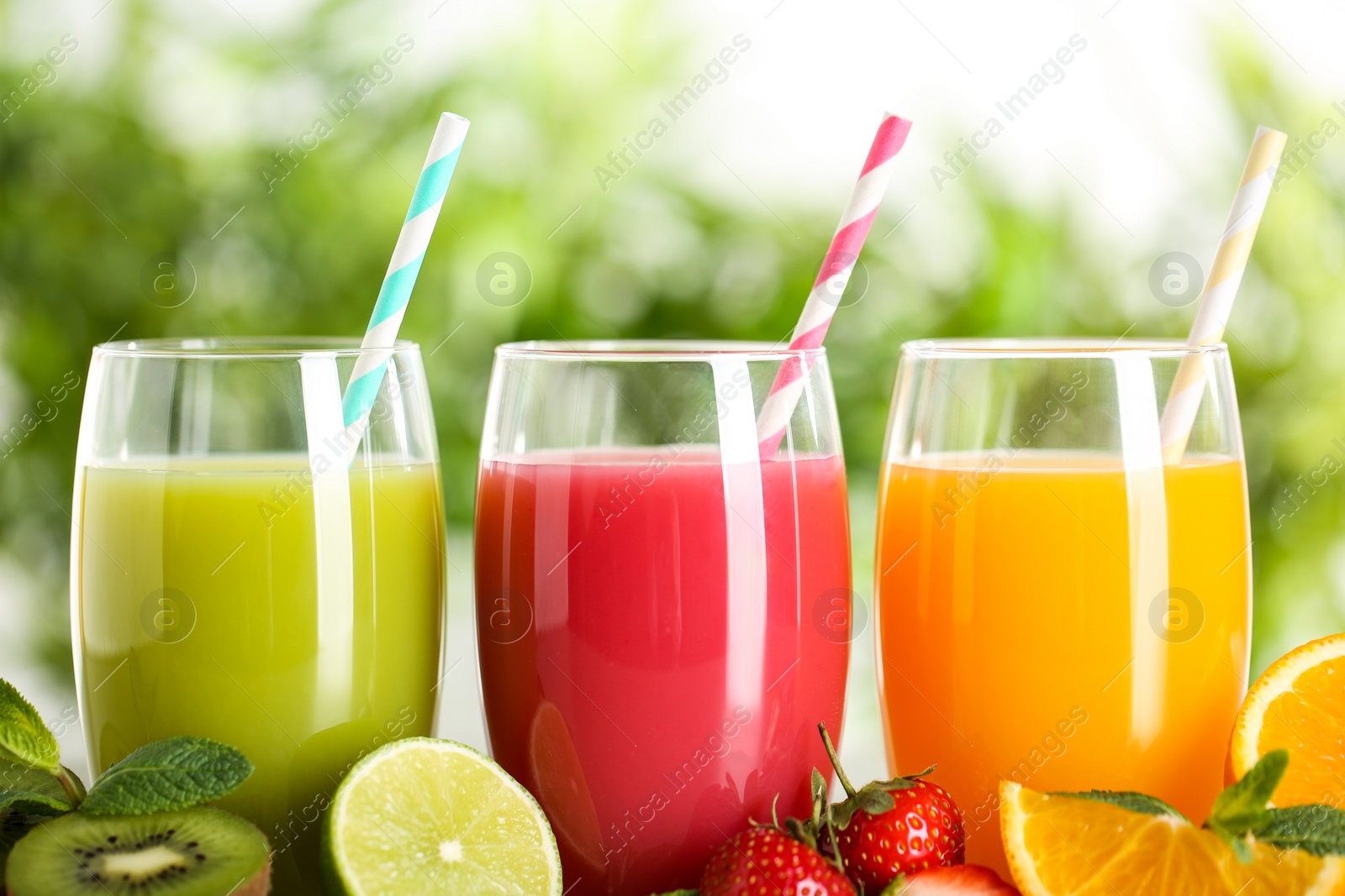 Photo of Glasses of different juices with straws and fresh fruits on blurred background