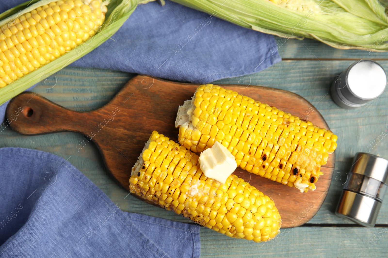 Photo of Fresh grilled corn cobs with butter on blue wooden table, flat lay