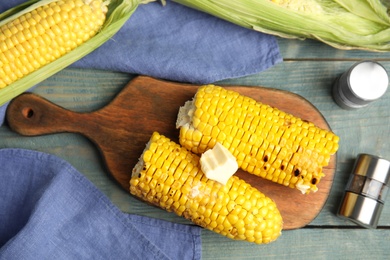 Photo of Fresh grilled corn cobs with butter on blue wooden table, flat lay