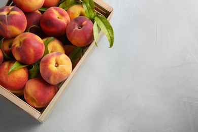Photo of Fresh sweet peaches in wooden crate on light table, top view. Space for text