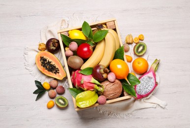 Crate and different exotic fruits on white wooden table, flat lay