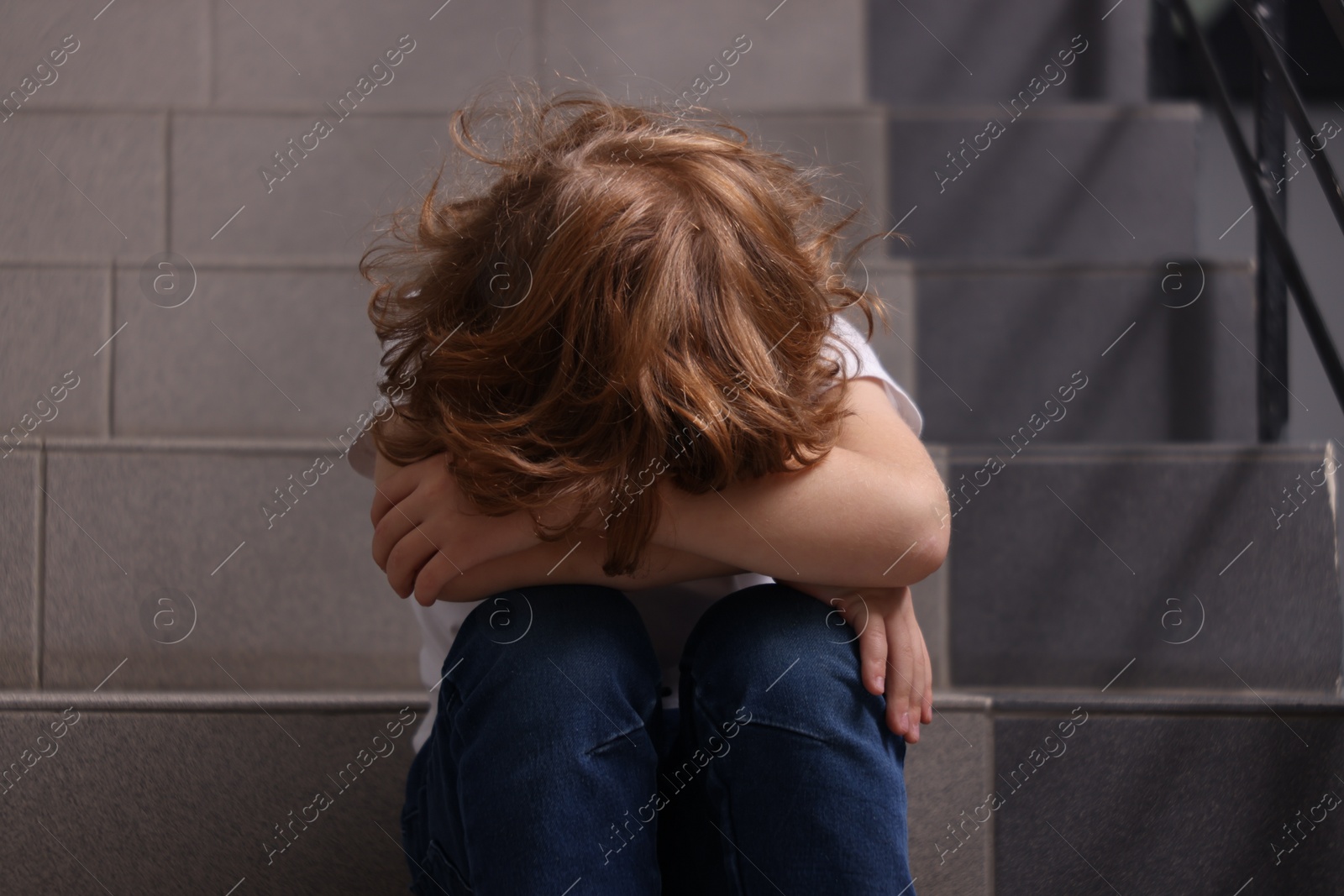 Photo of Child abuse. Upset boy sitting on stairs