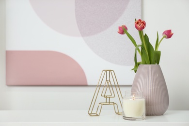 Photo of Vase with beautiful tulips, burning candle and decorative letter on table indoors, space for text. Interior elements