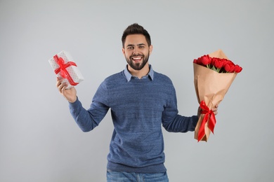 Happy man with red tulip bouquet and gift box on light grey background. 8th of March celebration