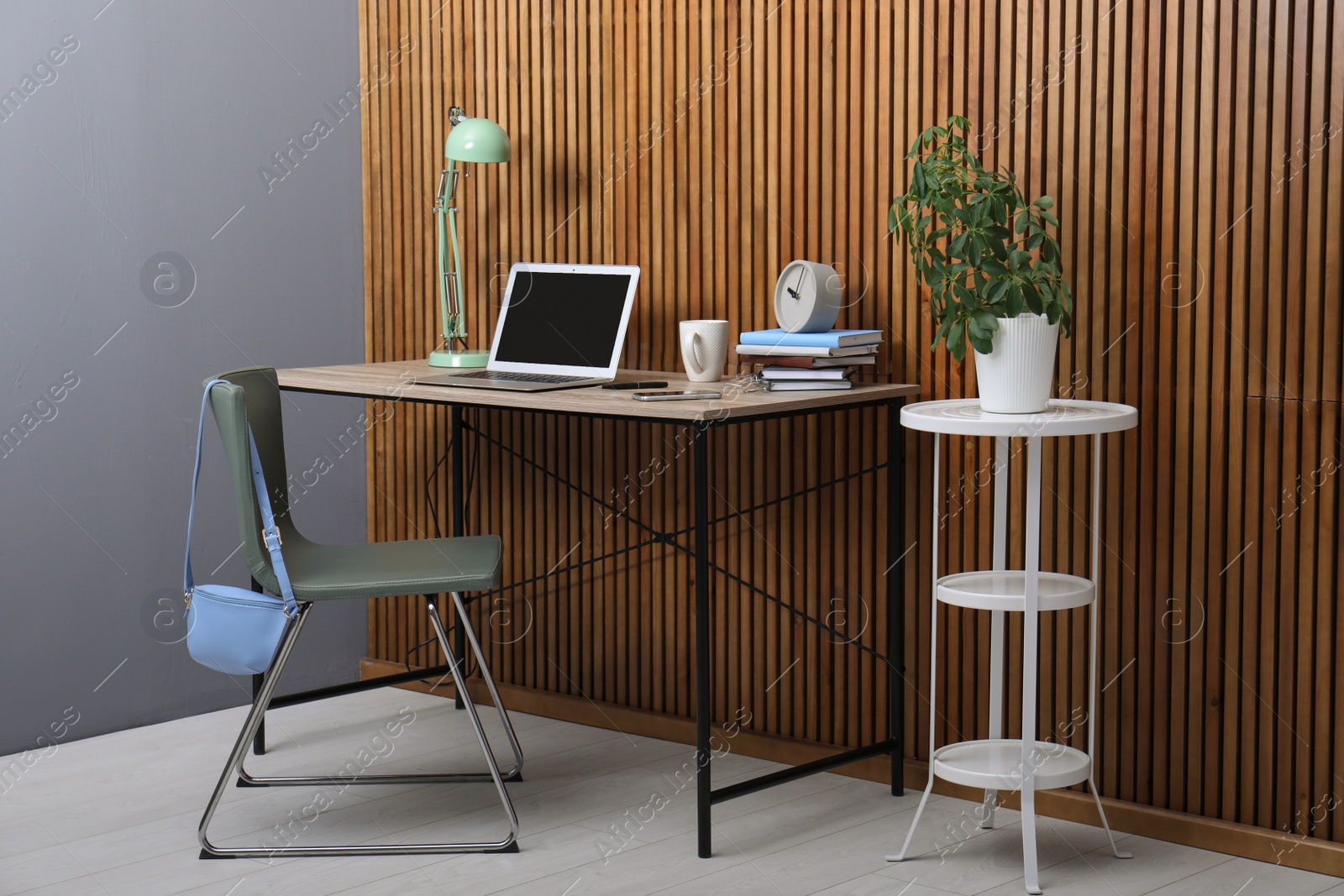 Photo of Stylish workplace interior with laptop on table near wooden wall. Space for text